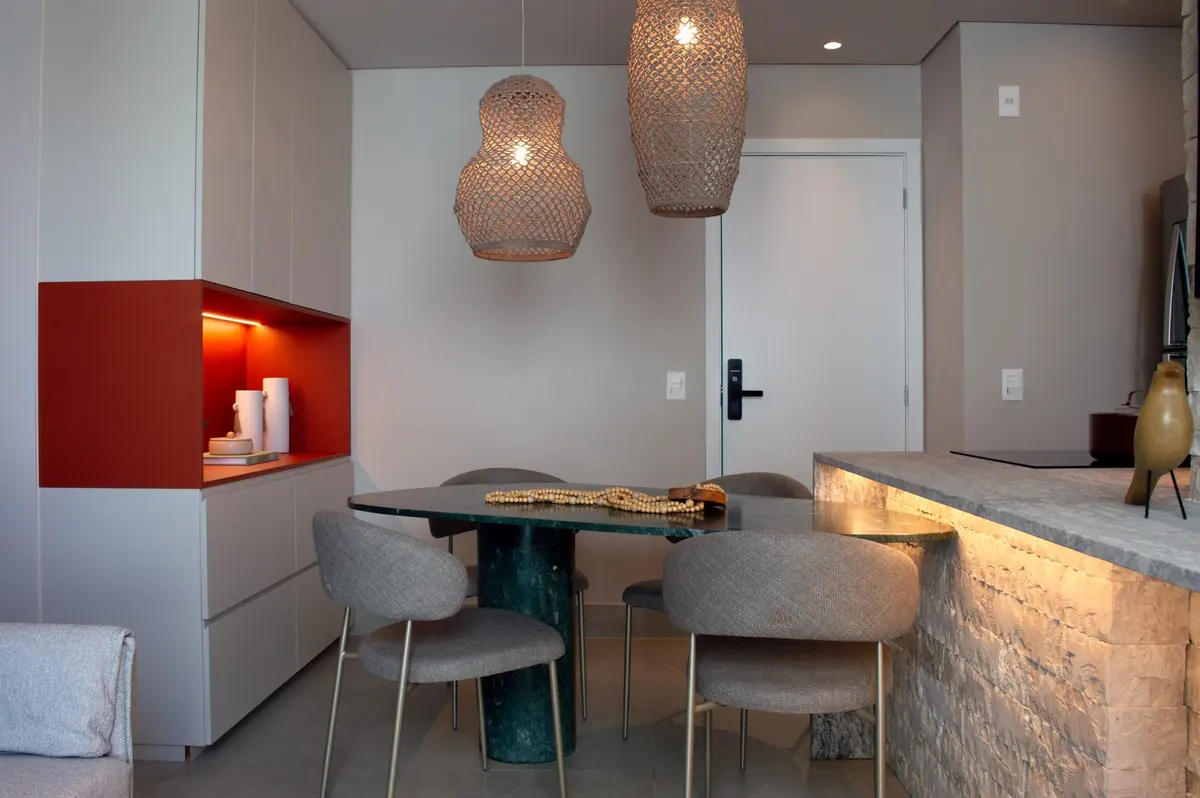 Sala de jantar com nicho laranja iluminado, mesa de mármore verde e luminárias de fibra