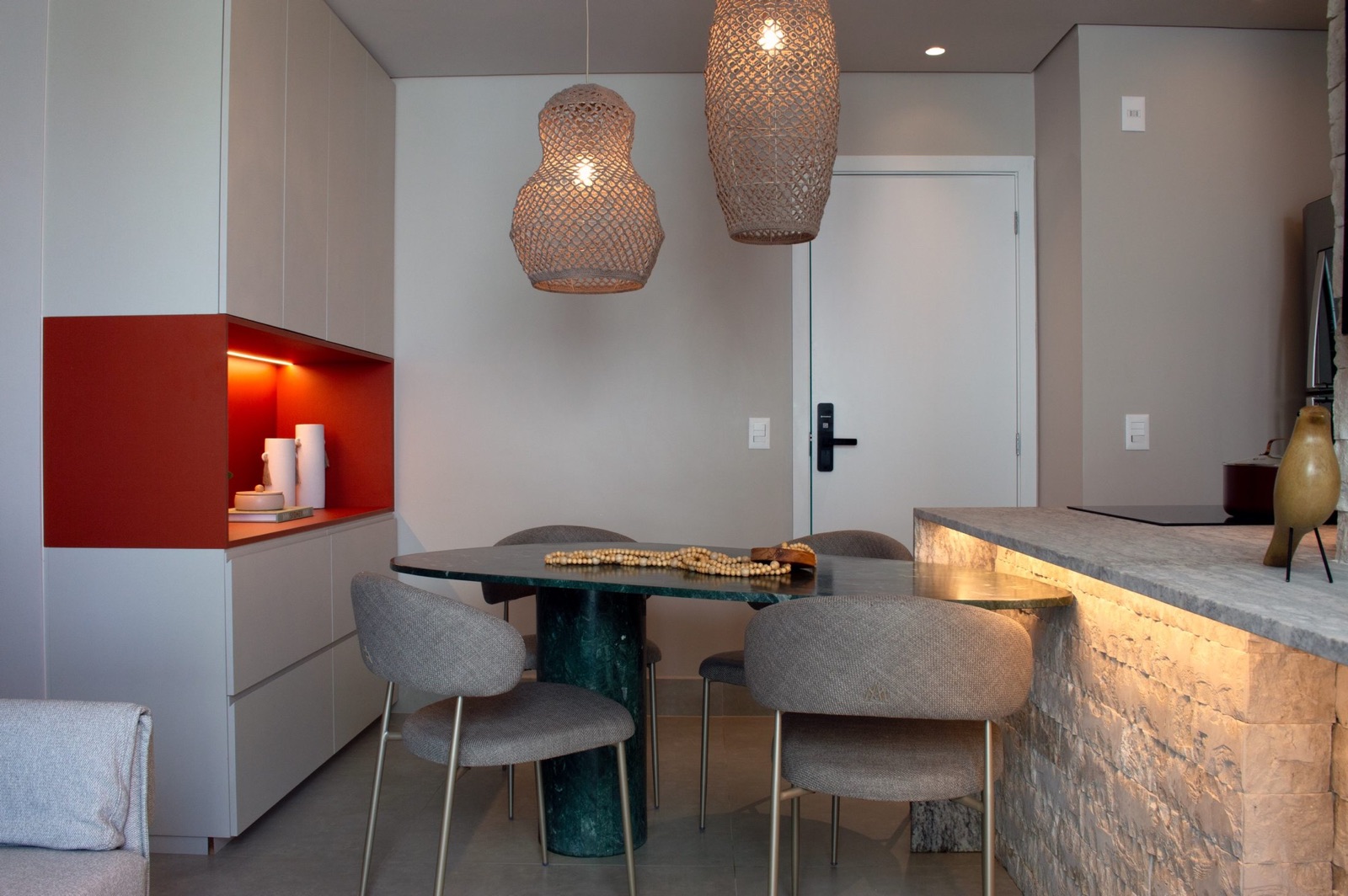 Sala de jantar integrada com mesa de mármore verde, nicho laranja iluminado e bancada em pedra natural com luz indireta